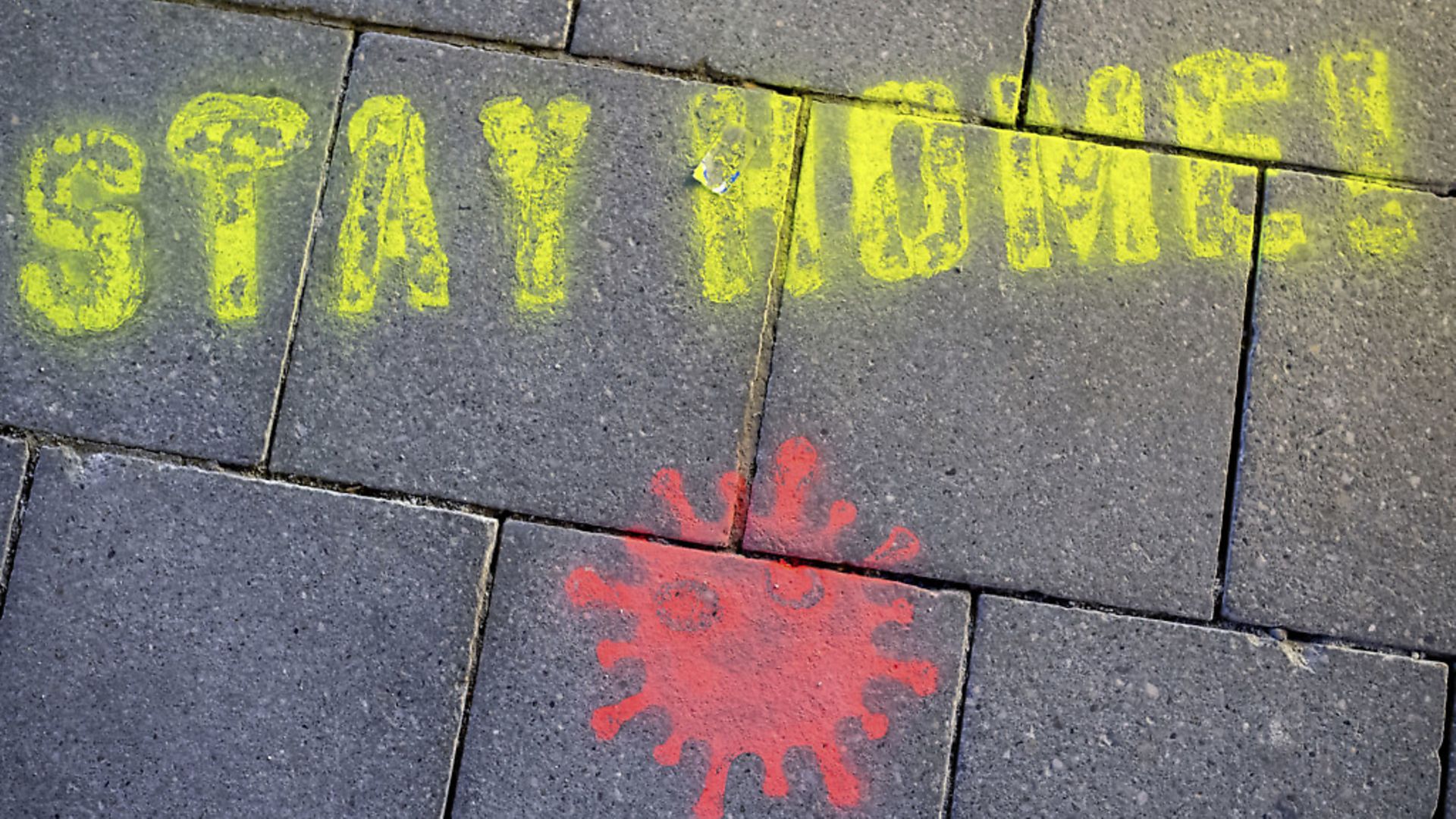 A graffiti consisting of the text "Stay Home" and a symbolic novel coronavirus has been sprayed on the ground in Munich, Germany. (Sven Hoppe/dpa via AP) - Credit: AP