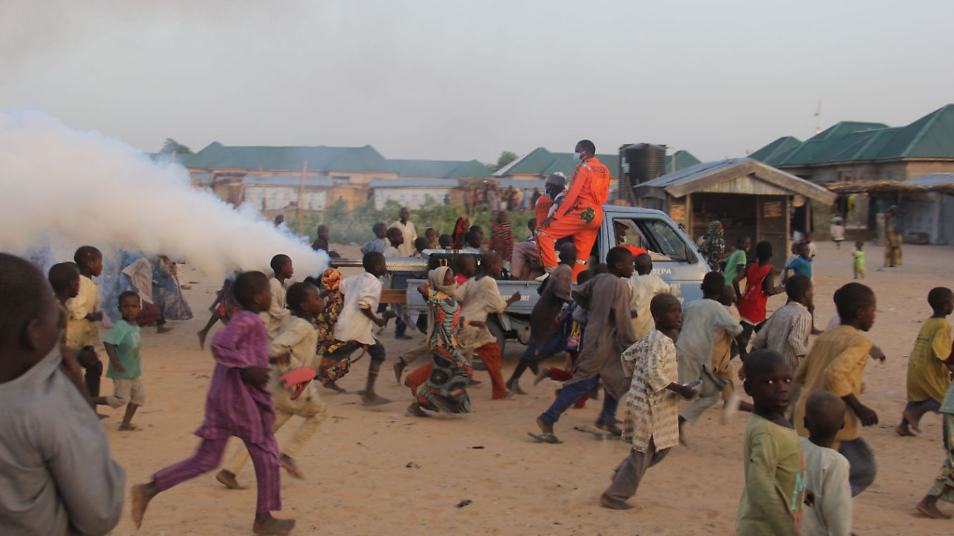 Children playfully run away from a fumigation machine mounted on the back of a pick up used in a displaced camp in Maiduguri. Picture: AUDU MARTE/AFP via Getty Images - Credit: AFP via Getty Images