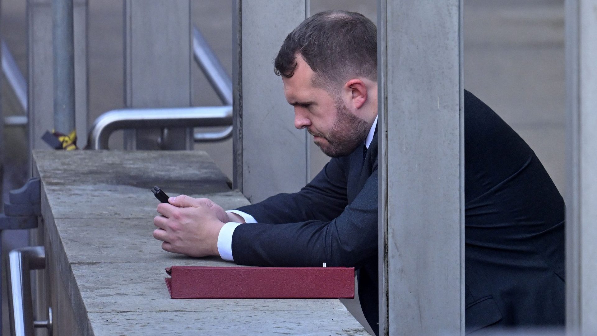 Jonathan Gullis uses his mobile phone as he leans on a wall outside the Houses of Parliament. Photo: JUSTIN TALLIS/AFP via Getty Images