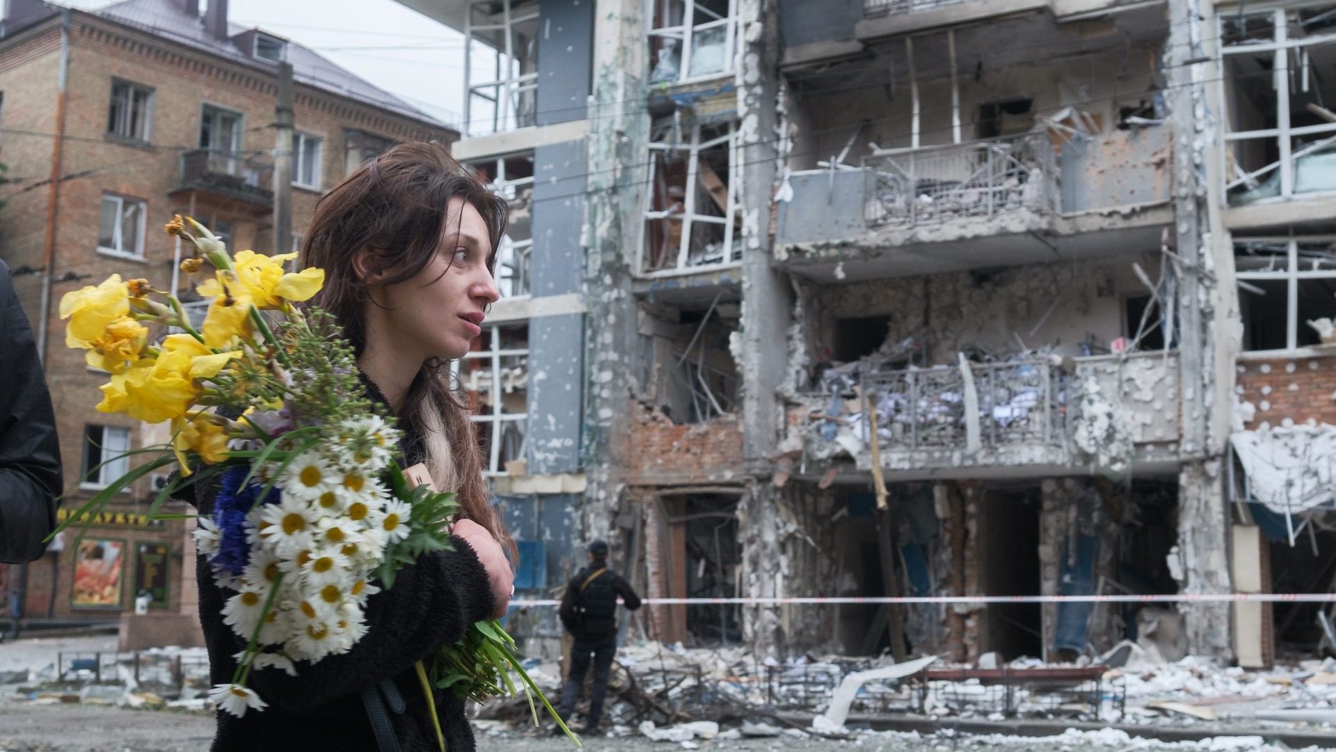A woman with a bouquet of flowers walks past a high-rise residential building in the Shevchenkivskyi district heavily damaged by a Russian drone strike on May 25 in Kyiv. Photo: Vitalii Nosach/Global Images Ukraine via Getty Images