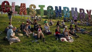 Festivalgoers sit on a hill in the evening sunshine beside a large Glastonbury sign overlooking the campsite on the first day of the 2013 Glastonbury Festival. Image: Andrew Cowie/AFP/Getty