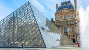 On a sunny summer day in the courtyard of the Louvre, the glass Pyramid is cleaned using both manual labour and a motorised robotic machine named Gekko. Image: Adobe