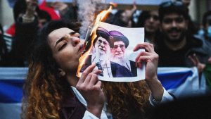 An anti-Iranian regime protester lights a cigarette with a burning paper depicting Iran’s supreme leader Ali Khamenei during a gathering outside the US Consulate in Milan on January 13, 2026. Image: by Piero Cruciatti/AFP via Getty Images